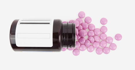Pink vitamins spilling from brown plastic bottle.