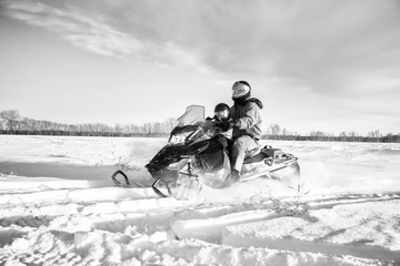 A father and his toddler daughter riding across a snow covered field in a black and white winter...