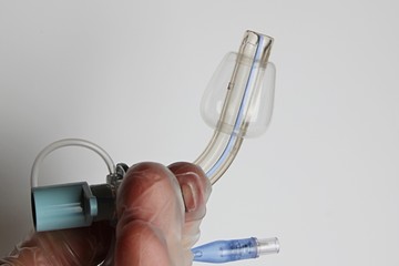 Tracheostomy tube held in left hand in glove, inflated polyurethane transparent conical cuff