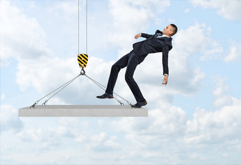 Businessman falling from the concrete slab suspended on the construction crane hook.