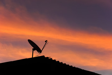 Skyscape in evening with silhouette roof and  satellite dish.