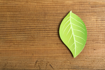 Green paper leaf on old wood background.