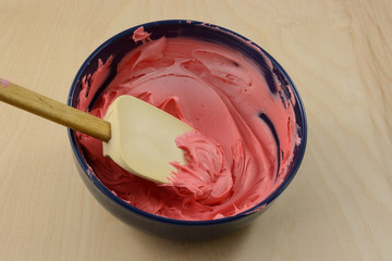 Mixing red frosting in blue bowl with spatula