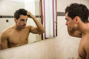 Handsome man looking at his face in mirror, checking hair and hairline