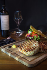 Grilled chicken burger on wooden board with wine bottle and glass