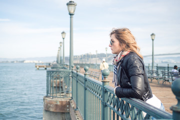 Fototapeta premium Young attractive serious woman standing on the bridge, looking at the distance with mixed emotions, reflecting on something, disappointed, maybe frustrated.