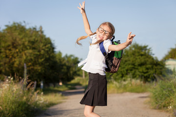 Smiling young school girl in a school uniform jumping on the roa