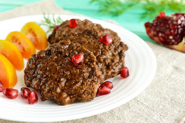 Juicy liver cutlets with pomegranate seeds on a white plate. Close up