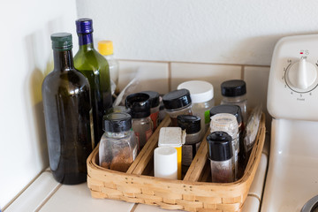 Green glass bottle with olive oil, jars of spices, salt and peper on a tray in the kitchen near the...