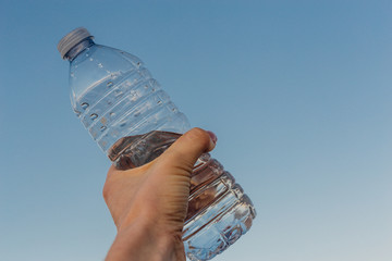 Female hand with a plastic bottle of water on a sky background