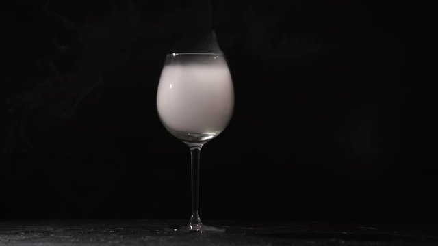 On a black background of transparent glass scattered white smoke. In a glass jar on a high pedicle is white steam. Suddenly he begins to move fast and extends beyond the edges. A cloud dissolves in