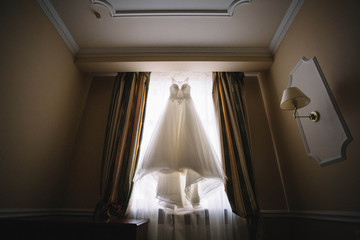 Fototapeta na wymiar Beautiful white wedding dress hanging on the window