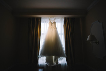 Fototapeta na wymiar Beautiful white wedding dress hanging on the window