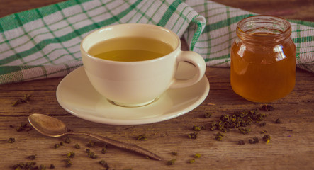 Green tea in a white cup and jar of honey with spoon and green k