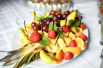 Fresh strawberries, ananas and oranges on black sticks