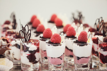 Glass shots with desserts of berries stand on mirror tray