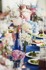 Little vases with field flowers and hydrangeas stand on blue din