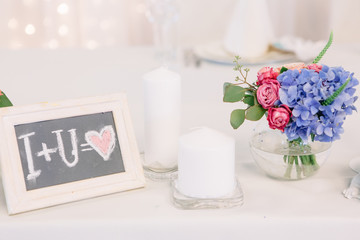 White frame with lettering 'I+U=love" stands behind white candle