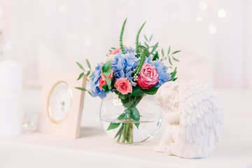 Vase with blue hydrangea and pink roses stands between white clo