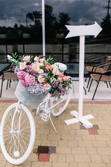 Fototapeta na wymiar Decorative white bicycle with basket and flowers stands in the r