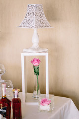 Square glass with pink rose bud stands before box with rose in a