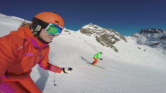 4k skiing footage, sideview selfie woman and man skiing down ski slope in mountains with blue sky
