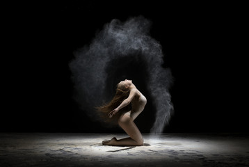 Fototapeta na wymiar Graceful girl posing in white dust cloud in studio