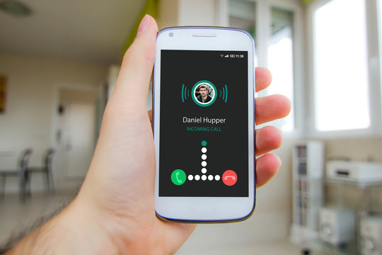 Man's hand holding smartphone with incoming call on the screen at home.