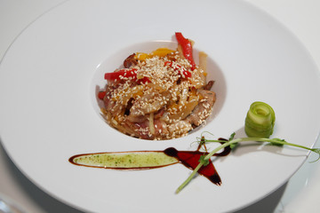 Salad of roasted meat with vegetables and red pepper, sesame seeds in a white plate.