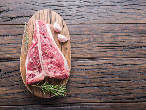 Steak T-bone with spices on the wooden cutting board.