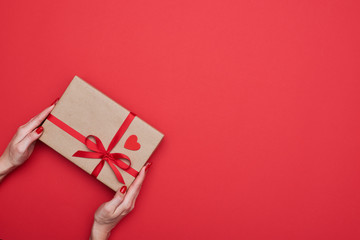 Hands diagonally holding present box wrapped with red ribbon