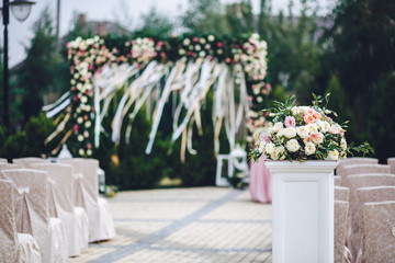 Fototapeta na wymiar White pillar with rose bouquet stands on the path to wedding alt