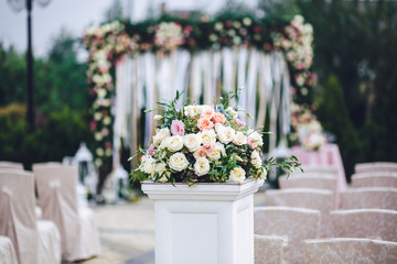 White pillar with rose bouquet stands on the path to wedding alt