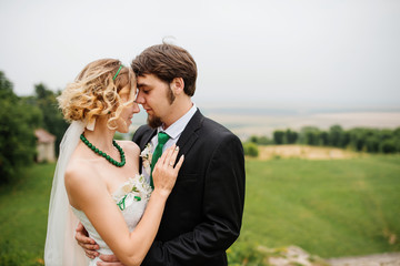 Embracing wedding couple in love on cloudy weather outdoor.