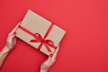Woman hands holding diagonally gift box wrapped with red ribbon