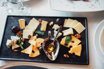 Steel bowl with honey stands on black dish with cheese and nuts