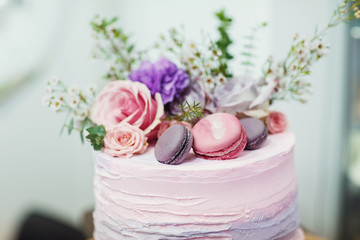 Pink and violet flowers and macaroons lie on top of tasty cake