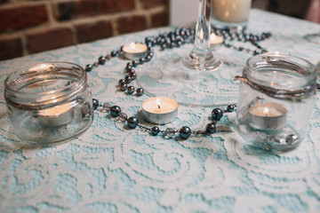 Obraz na płótnie Canvas Little white candles stand along chain of pearls on blue table