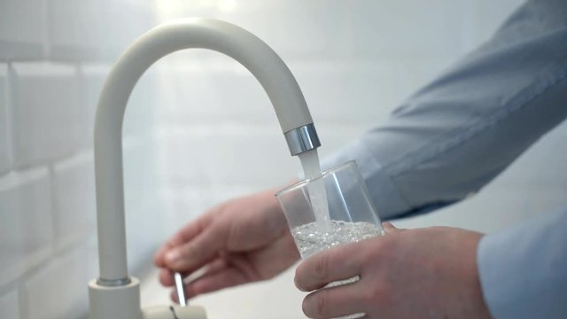 man pours water into a glass from a faucet 