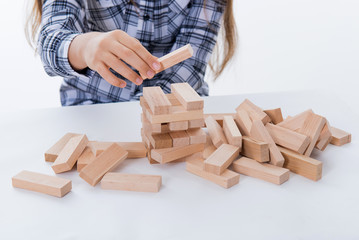 Girl playing Jenga. Entertainment activity. Education, development. Game of physical and mental skill. Removing blocks from a tower. Keep balance. girl builds tower of wood blocks 
