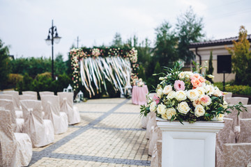 Pillar with bouquet of beige roses stands before the path to wed