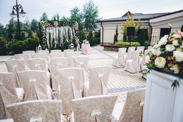 Chairs covered with beige cloth stand in rows before wedding alt