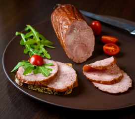Smoked sausage, ham with red tomatoes and herbs on a dark plate