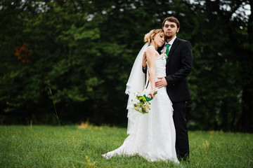 Embracing wedding couple in love on cloudy weather outdoor.