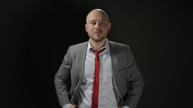 Bald man in a suit raises his head and looks at the camera. the average plan. on a black background.