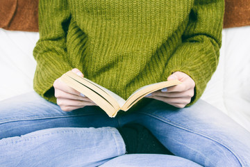 Persona con jersey verde y vaqueros leyendo un libro 