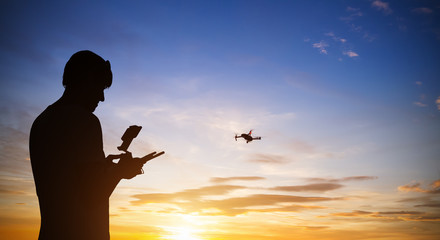 Drone pilot with quadrocopter. Silhouette against the sunset sky - obrazy, fototapety, plakaty