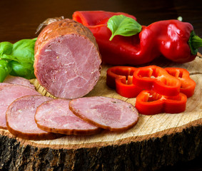 Smoked sausage, ham with red and green peppers and herbs on a dark background