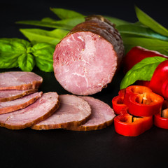 Smoked sausage, ham with red and green peppers and herbs on a dark background