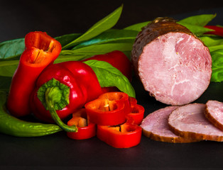 Smoked sausage, ham with red and green peppers and herbs on a dark background